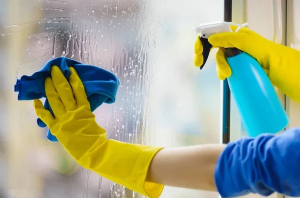 Hand in Handschuh reinigt Fenster mit einem Tuch